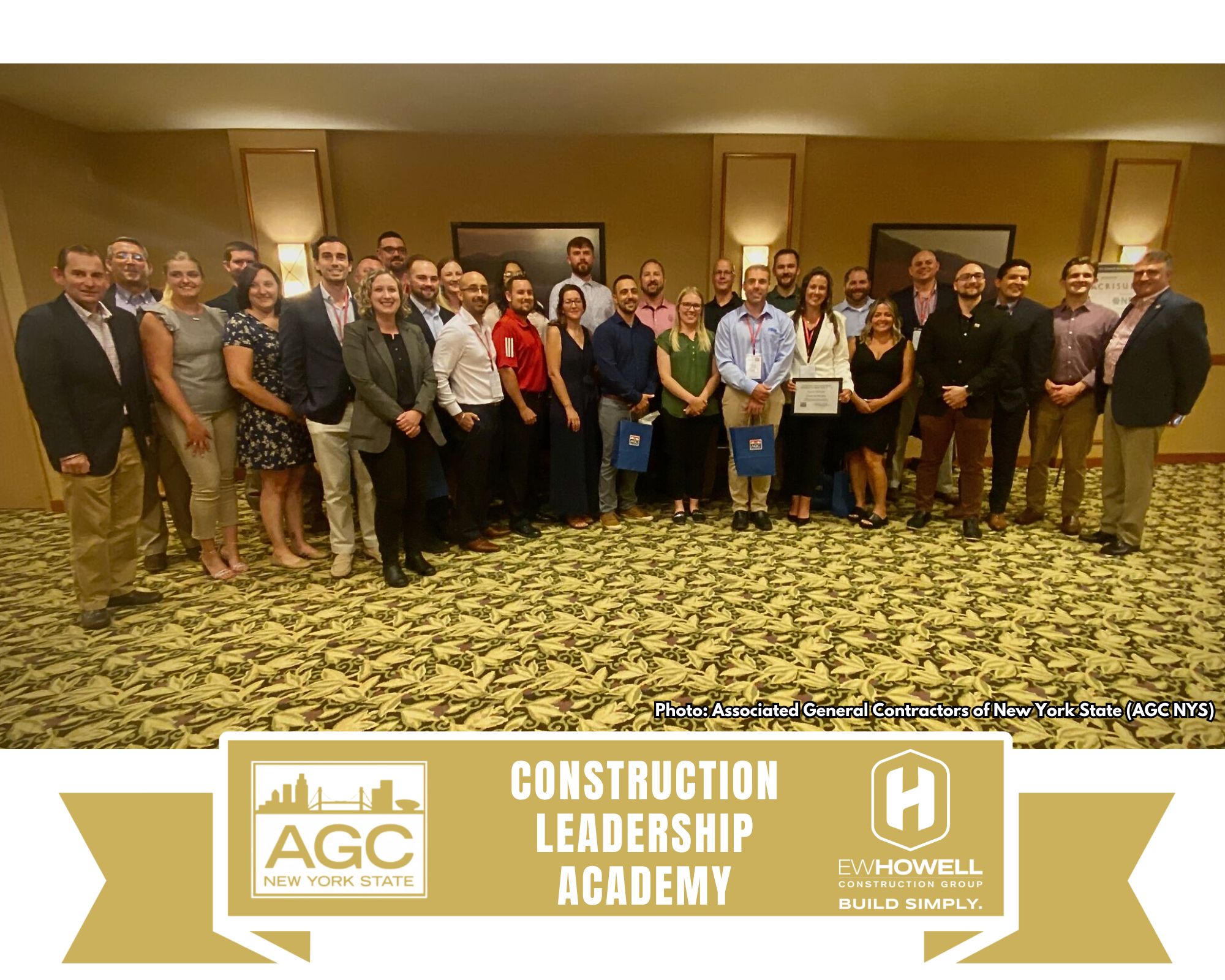 A group of about 25 people stands together indoors, smiling at the camera. Some hold certificates. A banner at the bottom reads "AGC New York State Construction Leadership Academy, E.V. Howell Construction Group.