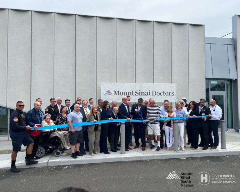 A large group of people, including officials and staff, stand in front of a Mount Sinai Doctors sign, holding and cutting a blue ribbon during a ribbon-cutting ceremony outside a modern building.
